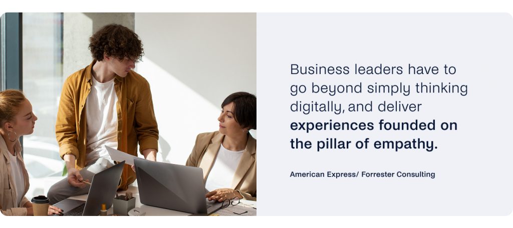 Three people are engaged in discussion at a table with a laptop and papers, illustrating how business leaders deliver empathetic experiences through conversational commerce.