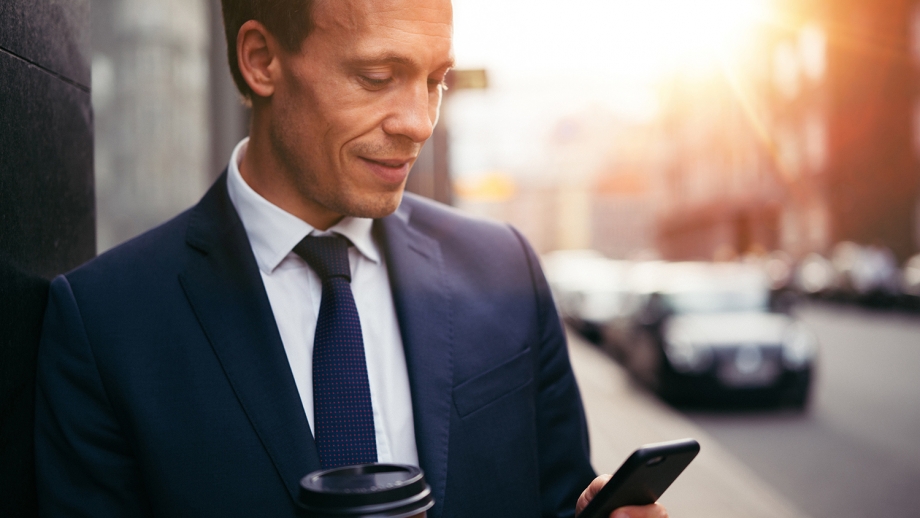 A man in a suit is holding a cup of coffee and checking messages on his phone related to WhatsApp Business.