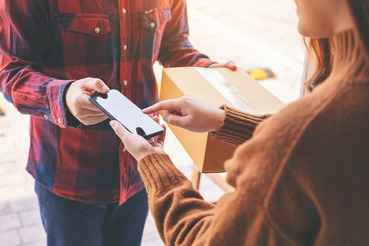 A man is handing a package to a woman using Whatsapp Business for Logistics.