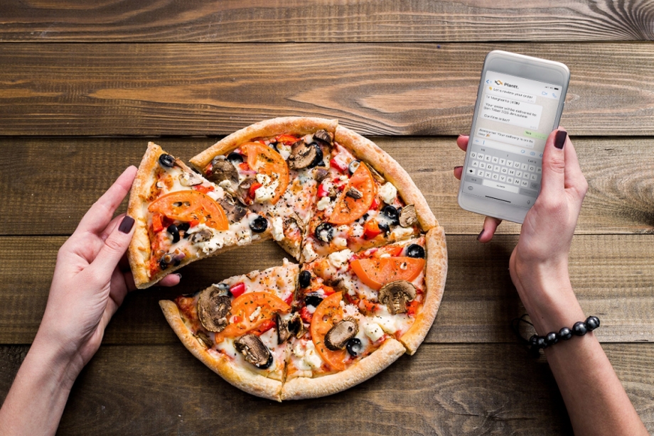 A woman is holding a phone while enjoying a slice of pizza.