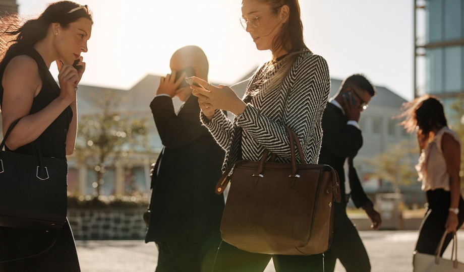 A group of business people walking down a street with their cell phones.