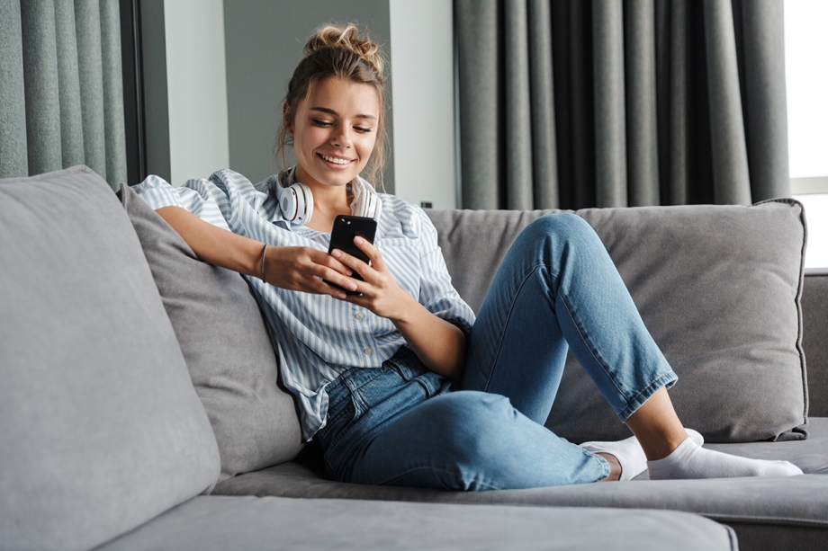 A young woman sitting on a couch engrossed in her cell phone, sending and receiving non-transactional messages.