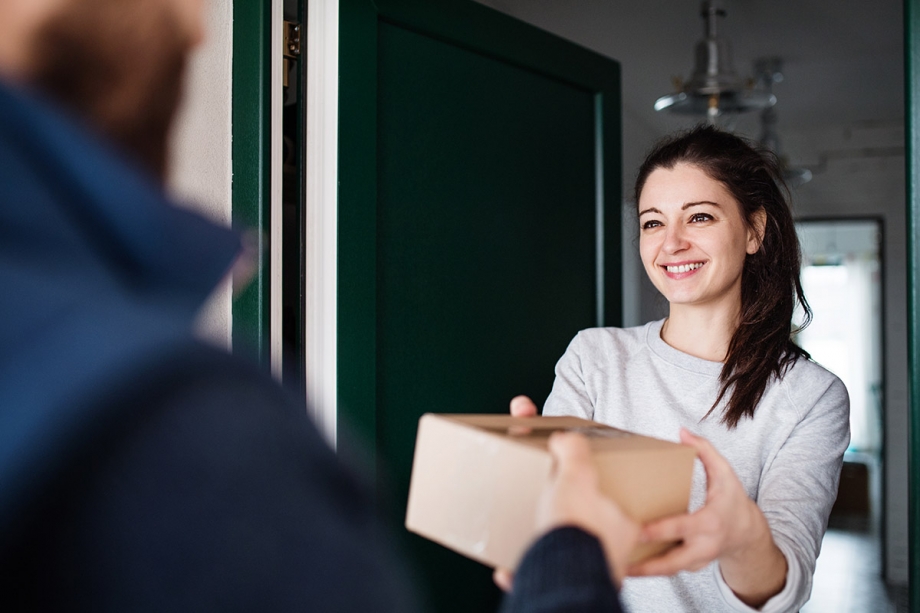 A woman delivering a package to a man in front of a door using WhatsApp Message Templates for Logistics.