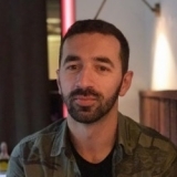 A man in a camouflage shirt sitting at a table, demonstrating how to send bulk messages on WhatsApp Business.