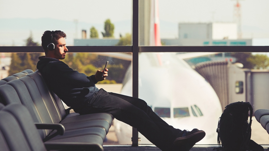 A man sitting on a bench in an airport, checking his Whatsapp messages on his phone while waiting for his business travel.