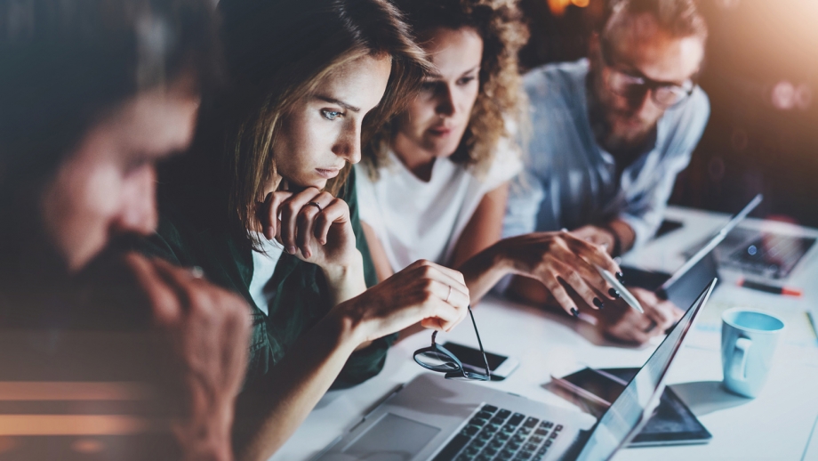 A group of people sitting around a table looking at laptops.