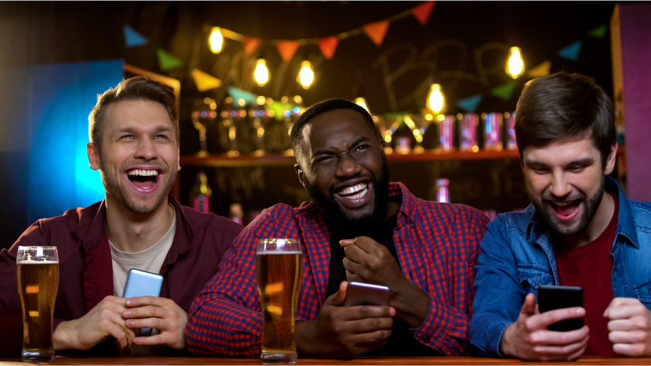 Three men are sitting at a bar looking at their phones.