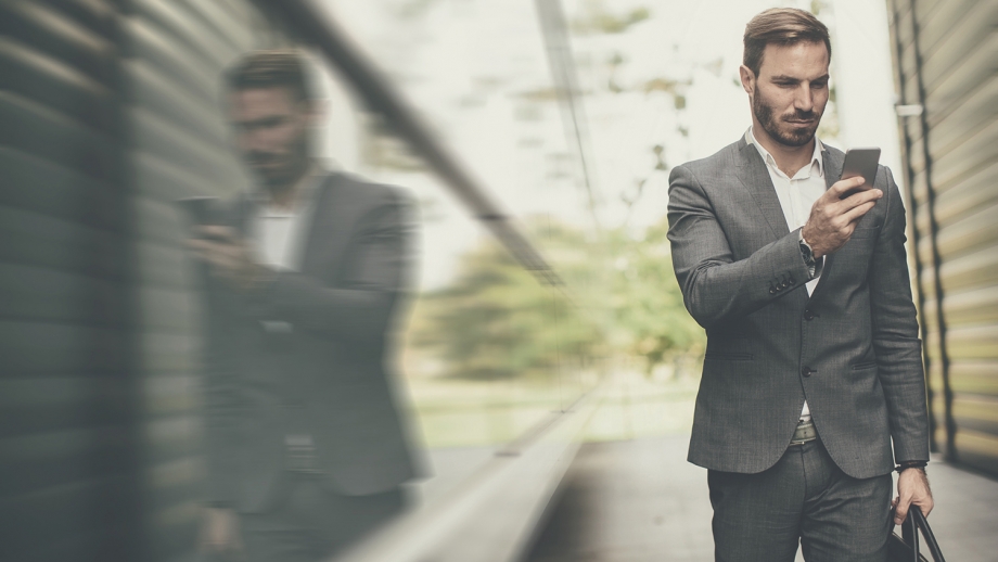 A man in a suit is looking at his phone, ensuring payment protection.