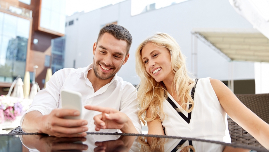 A young couple looking at their phone while sitting at an outdoor table.