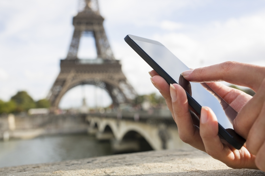 A hand holding a cell phone in front of the Eiffel Tower, using WhatsApp business for tourism.